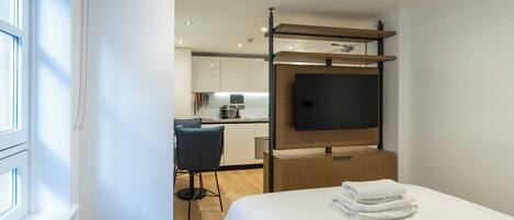 Une chambre d’hôtel moderne équipée d’un lit, d’un téléviseur fixé sur un panneau en bois, d’un petit coin cuisine et offrant une vue sur l’extérieur.