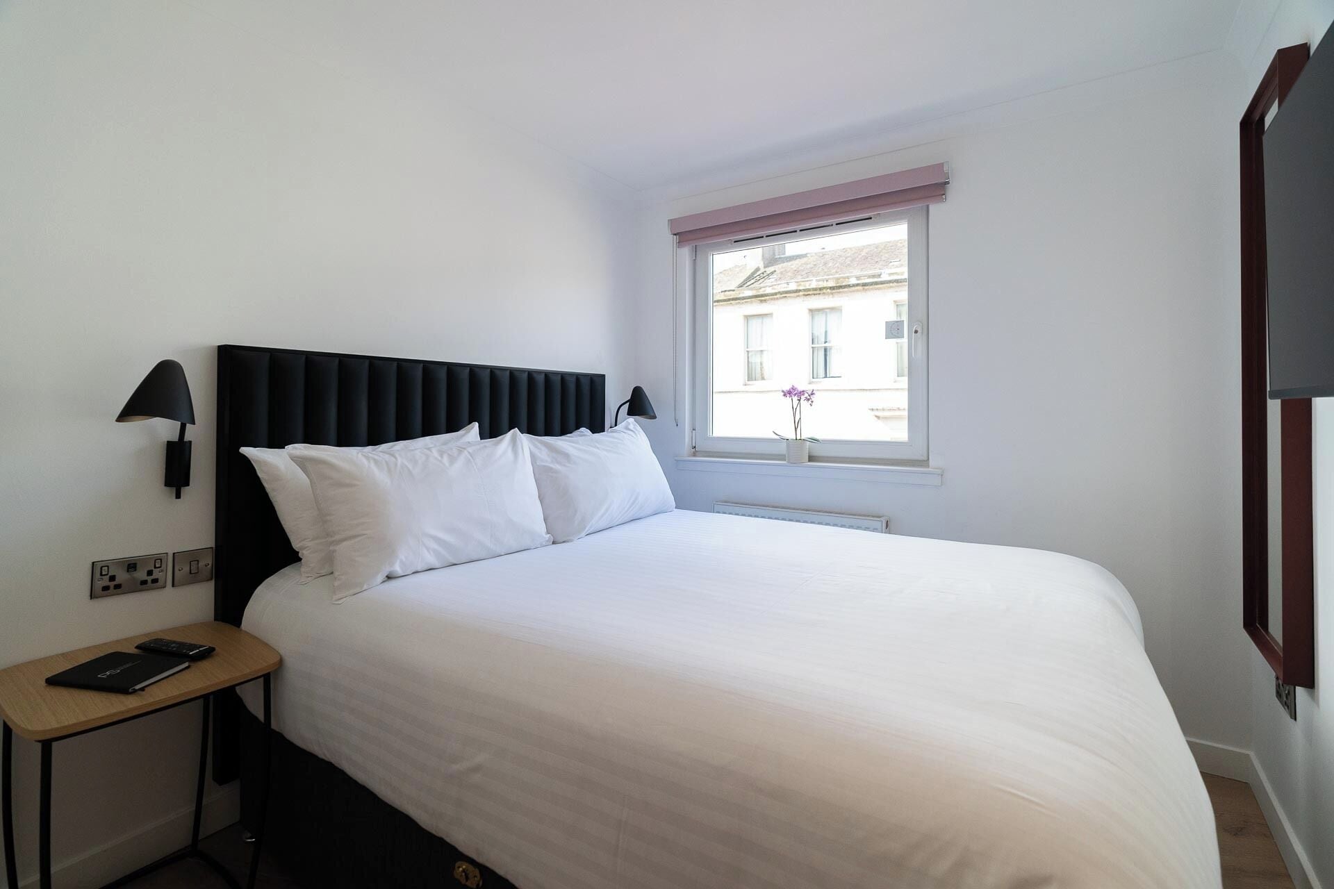 A neatly made bed with white linens, a black headboard, and a bedside table with a lamp and a book.