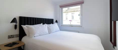 A neatly made bed with white linens, a black headboard, and a bedside table with a lamp and a book.