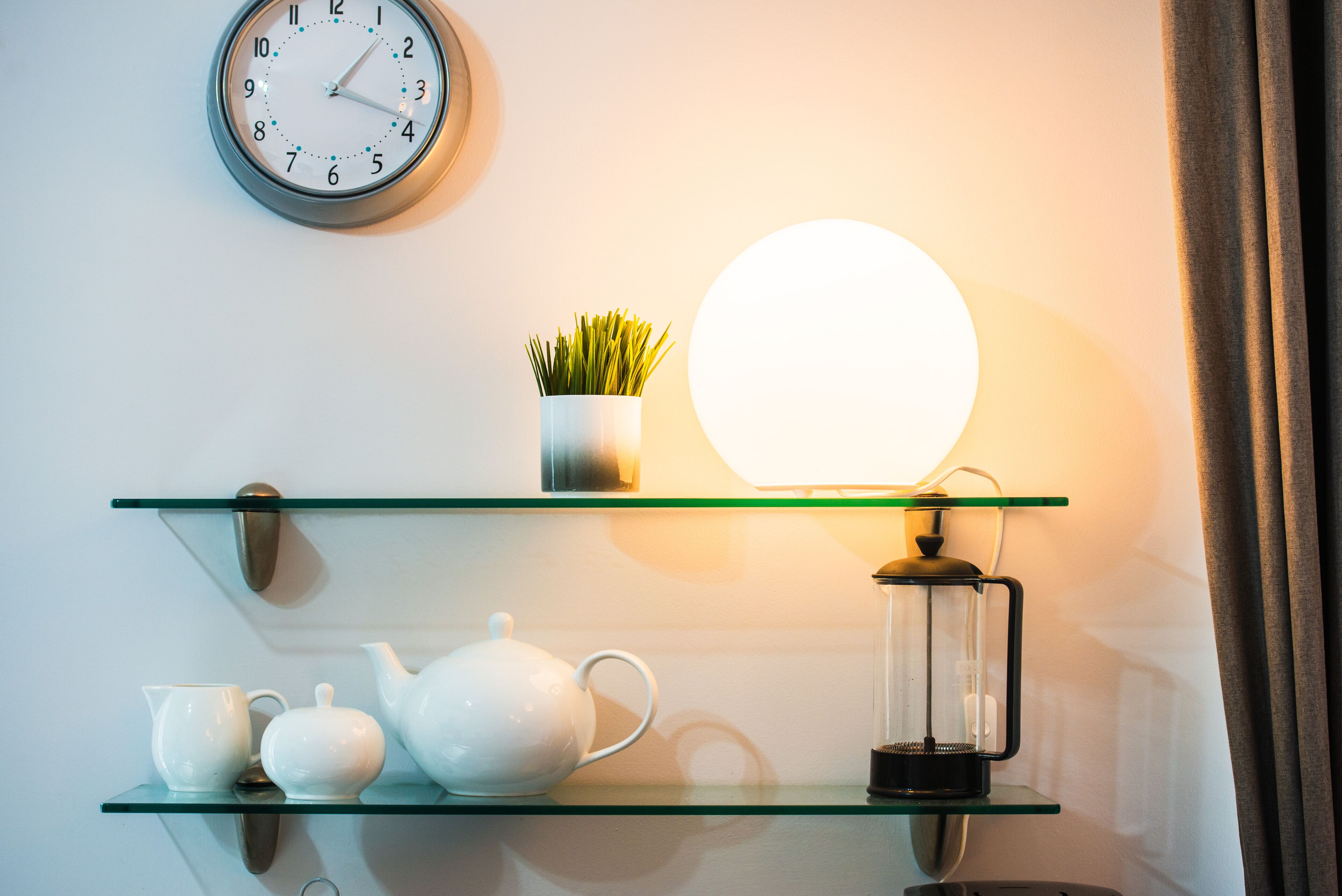 A wall-mounted clock, a potted plant, a tea set, and a lantern on a shelf.