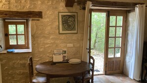 Un muro de piedra rústico con un cuadro enmarcado, una mesa de madera con sillas, una ventana y una puerta que da al exterior.
