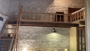 Una habitación con cama tipo altillo, una escalera de madera y una pared de piedra.