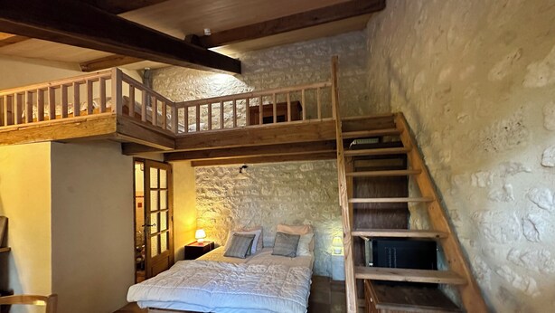 Un dormitorio con cama estilo loft, una escalera de madera y una pared de piedra.