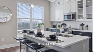 Una cocina moderna con armarios blancos, una isla central con asientos y un amplio ventanal que proporciona luz natural.