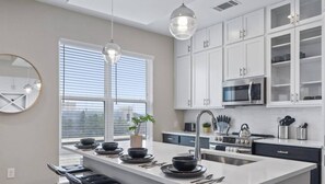 Una cocina moderna con armarios blancos, una isla central con asientos y un amplio ventanal que proporciona luz natural.