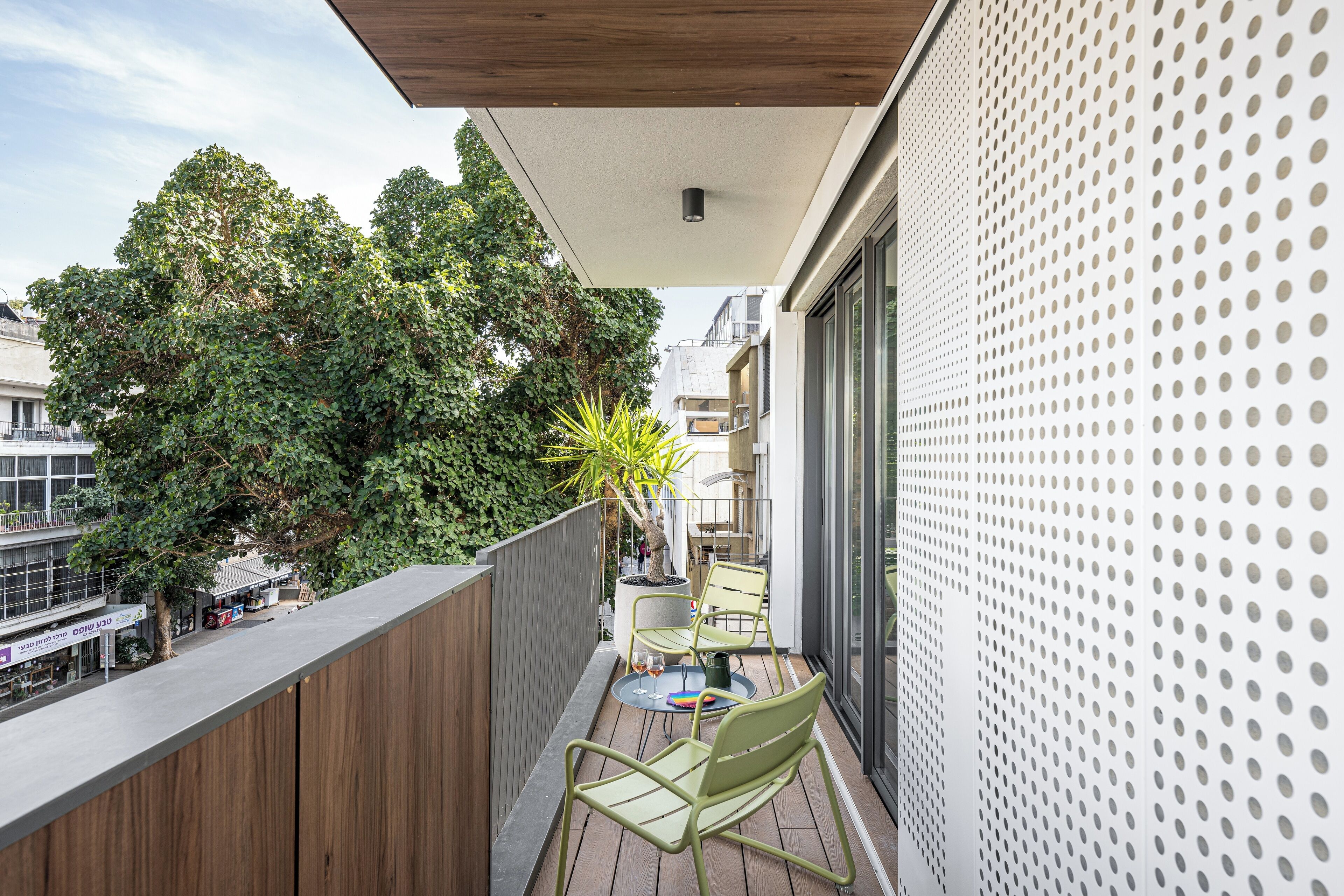 A balcony with a wooden floor, two green chairs, a small round table, and a potted plant.