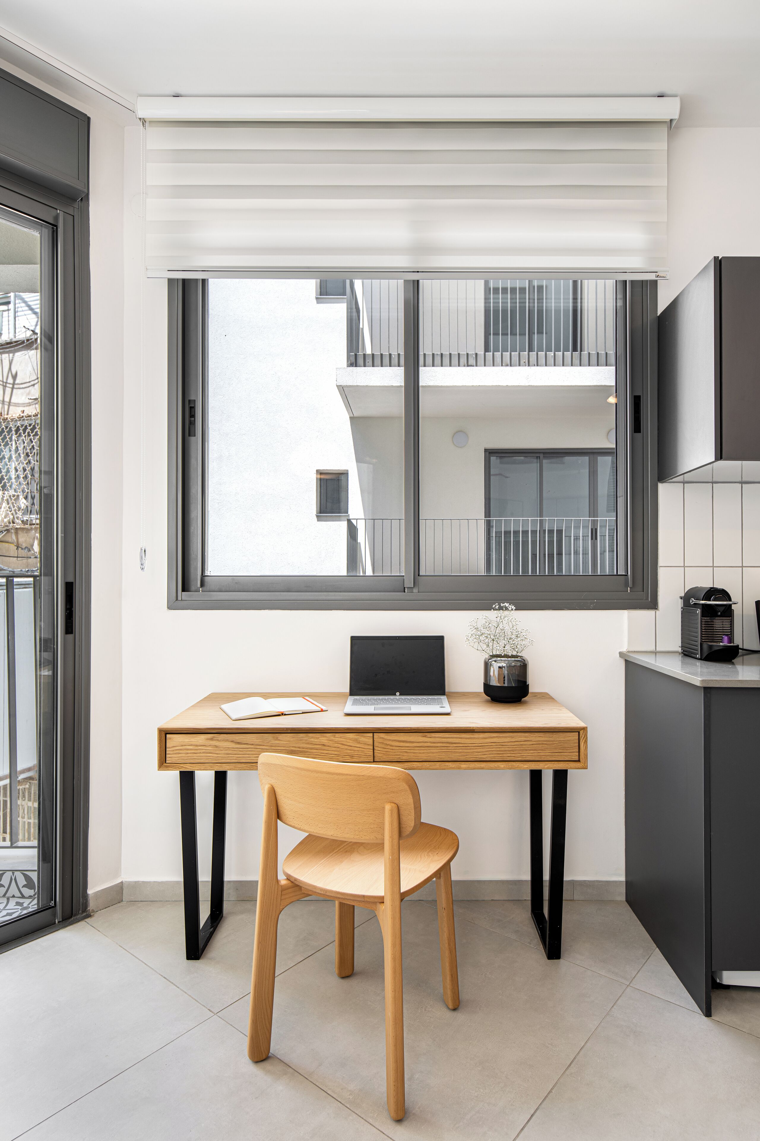 A modern kitchen with a wooden desk, a laptop, and a chair.