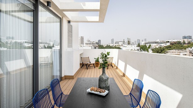 A balcony with a table, chairs, and a vase with flowers. - Mate GEORGE - By HOMY (Tel Aviv)