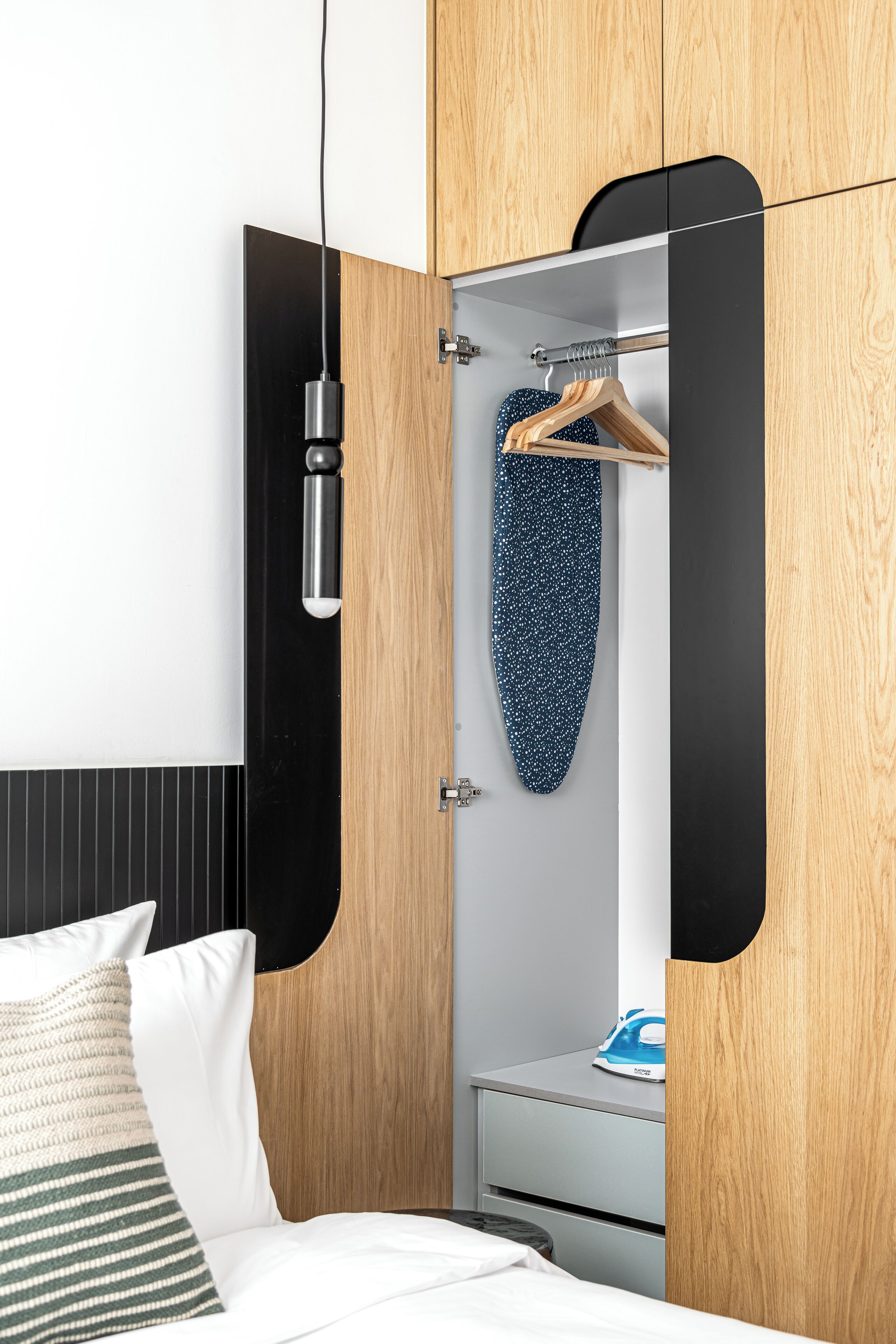 Une chambre à coucher moderne avec une armoire en bois, un portant à vêtements et une table de chevet avec un fer à repasser.