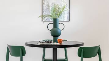 A round table with a dark metal base, surrounded by two green chairs. A vase with a plant is placed on the table.