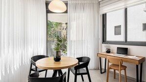 A modern room with a round wooden table, black chairs, a wooden desk with a laptop, and a large window with curtains. - Mate GEORGE - By HOMY (Tel Aviv)
