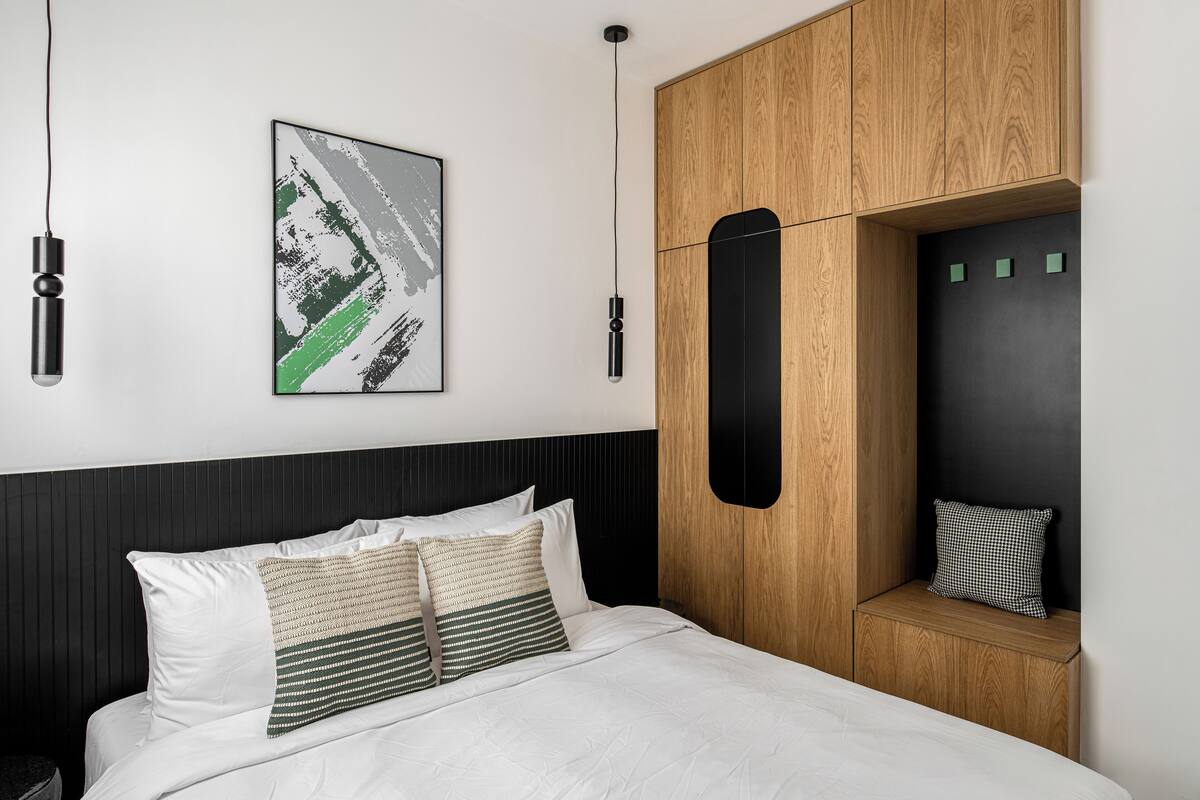 A modern bedroom with a bed, pillows, a wall-mounted artwork, and a wooden cabinet with a black panel.