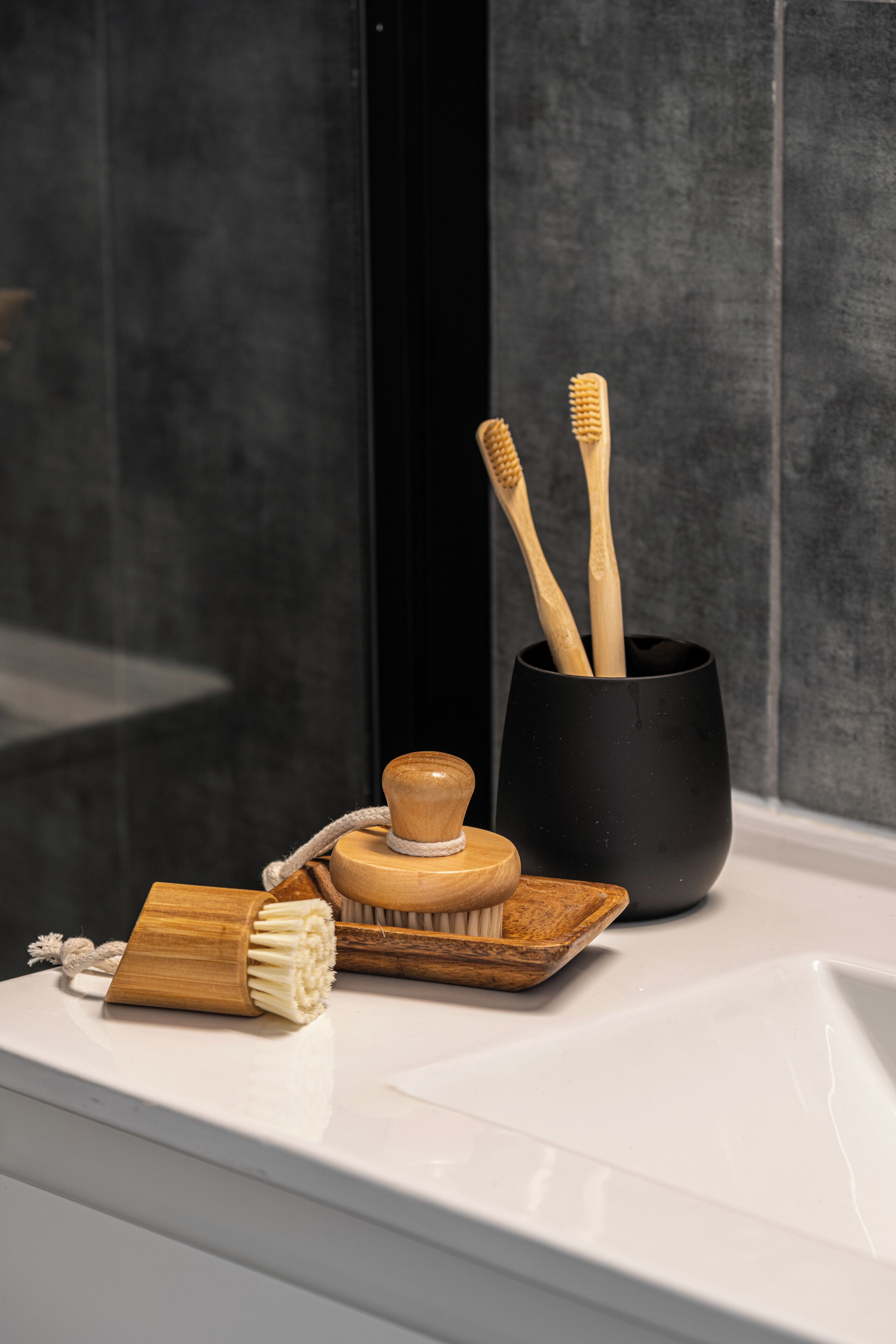A bathroom sink with a toothbrush holder containing two toothbrushes and a wooden brush.