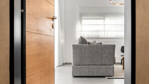 A modern interior with a wooden door, a grey sofa, and a 'WELCOME' mat. - Mate GEORGE - By HOMY (Tel Aviv)