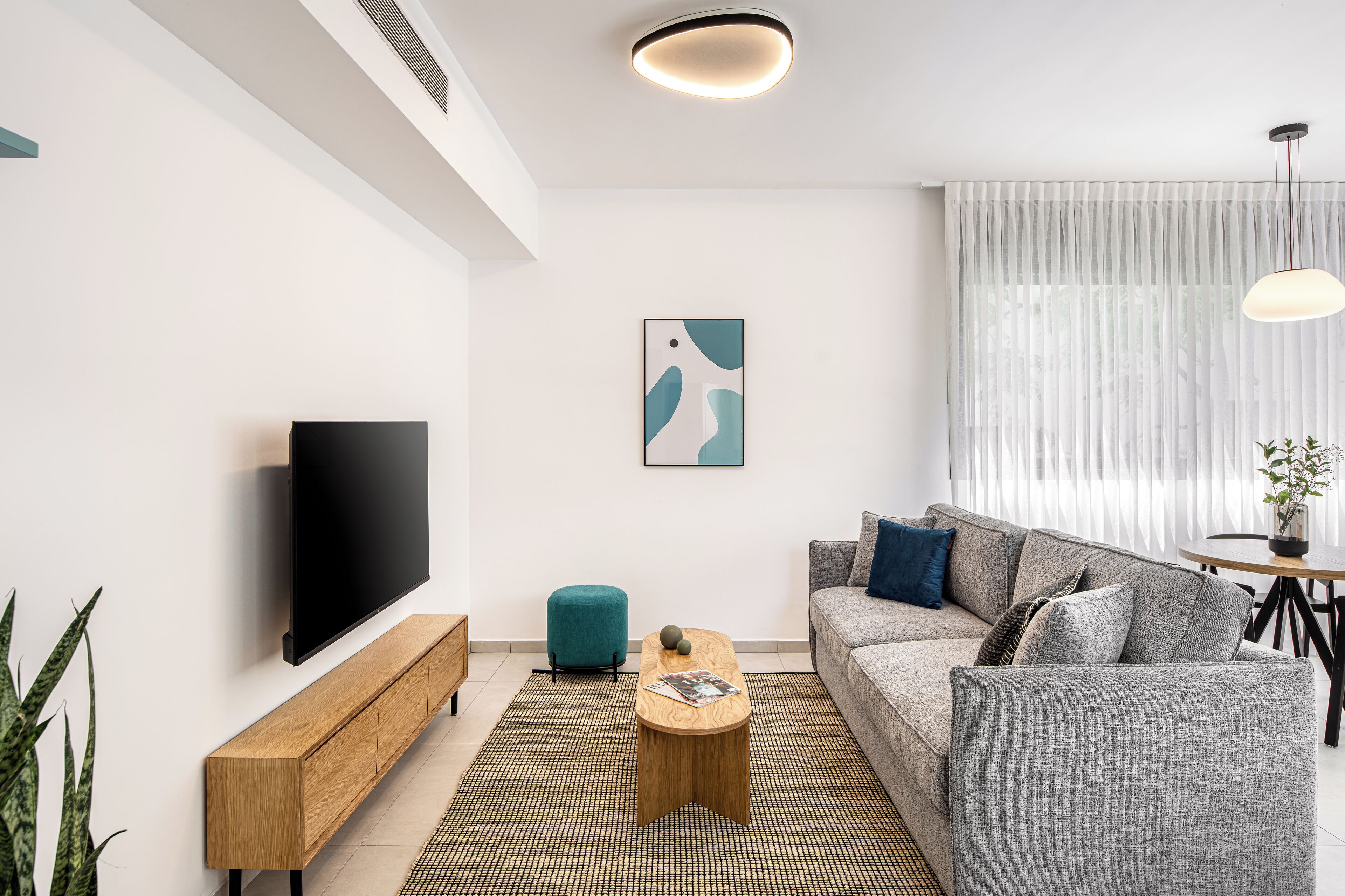 Uma sala de estar moderna com uma televisão de tela plana, um sofá, uma mesa de centro e uma pequena mesinha lateral.