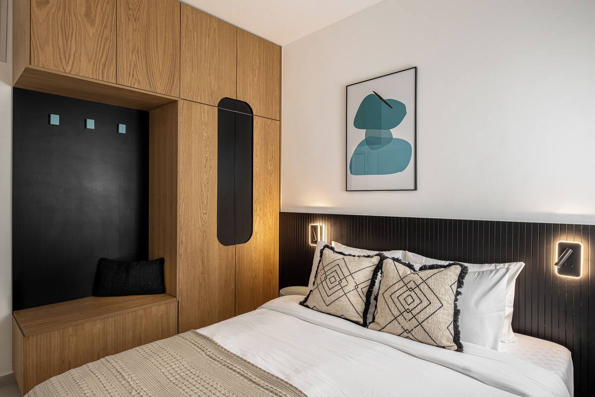 A modern bedroom with a bed, a built-in bench, and a wall-mounted light fixture.