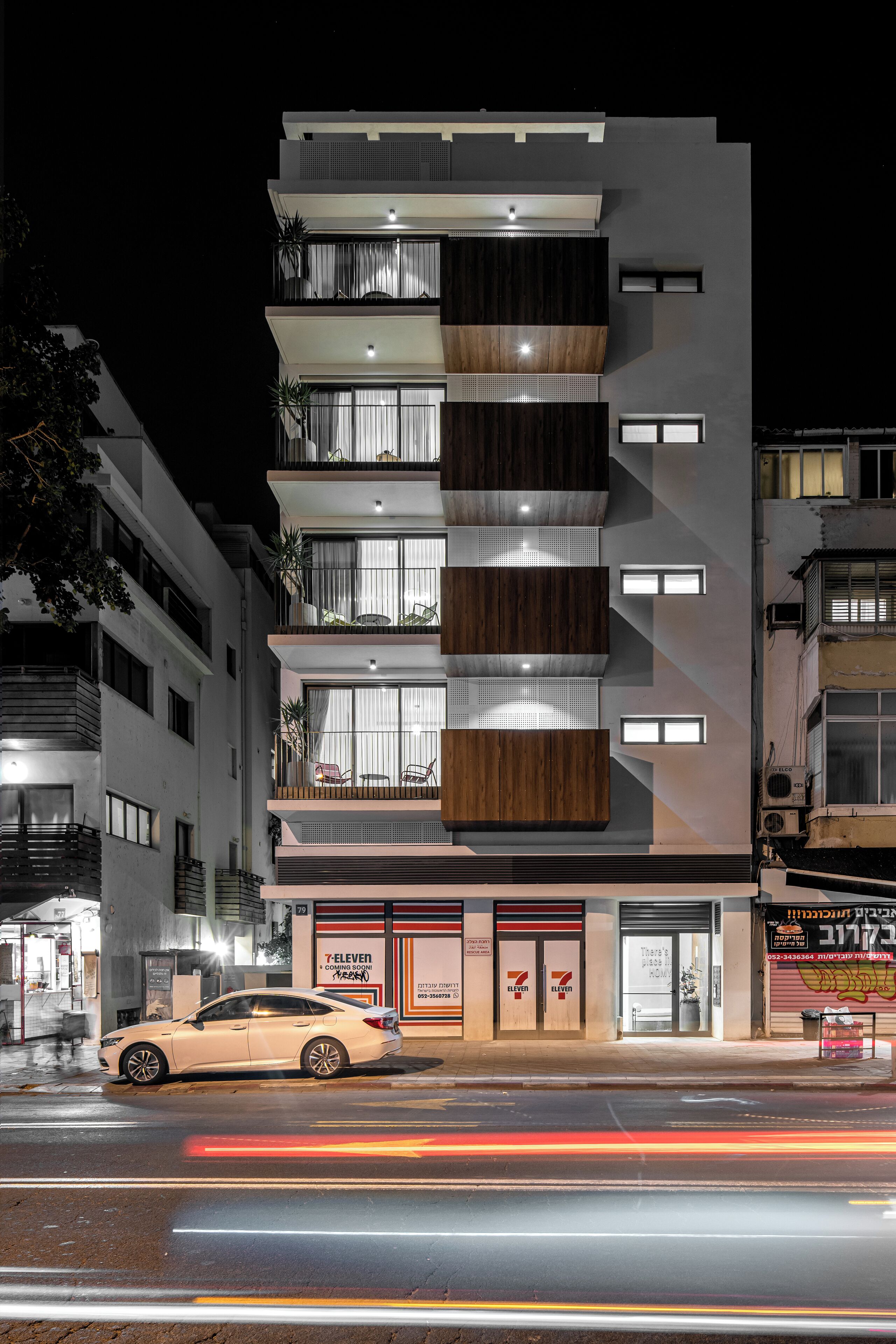 A multi-story building with a modern design, featuring balconies with plants and large windows.