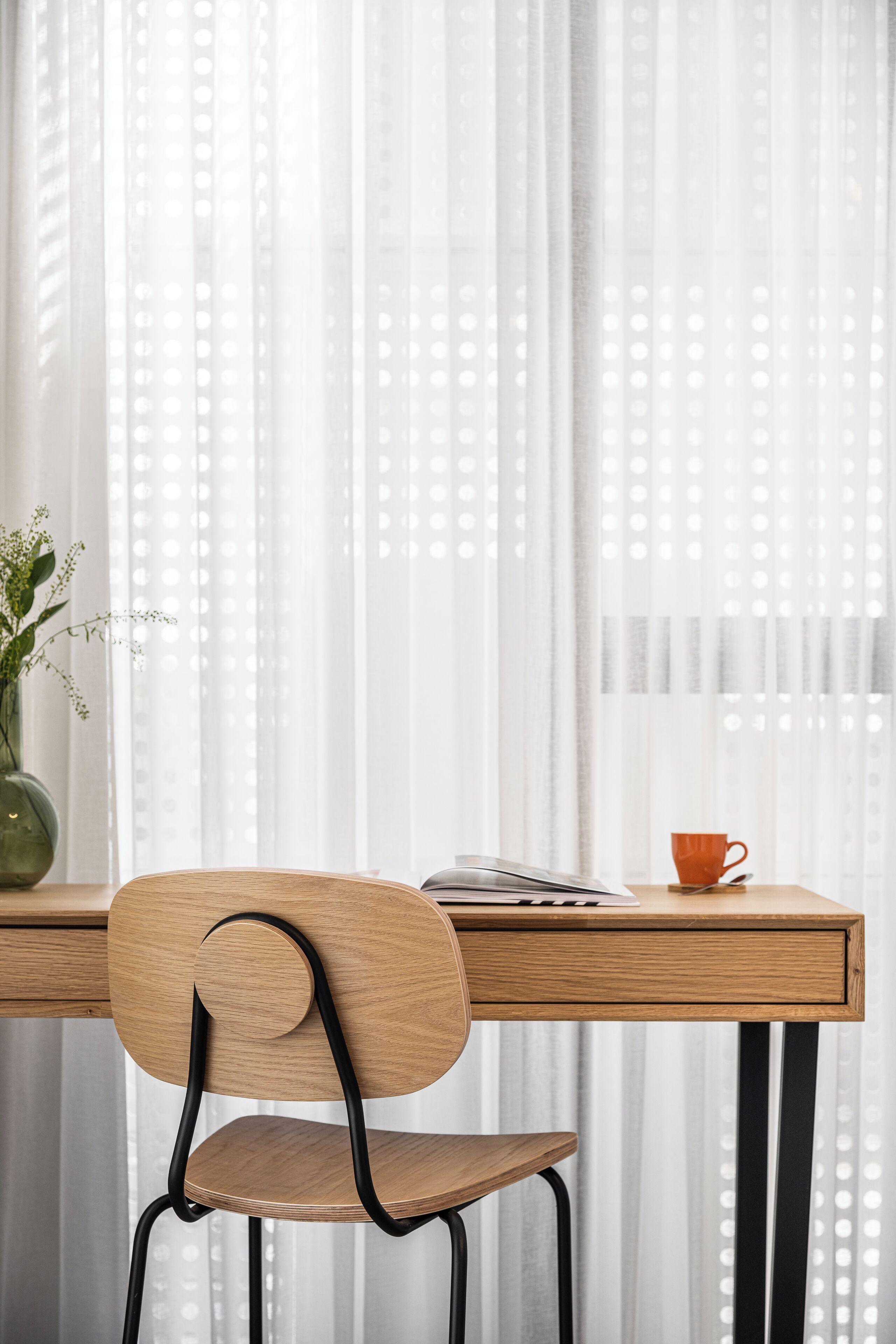 Un escritorio de madera con una silla, un jarrón con flores y una taza.