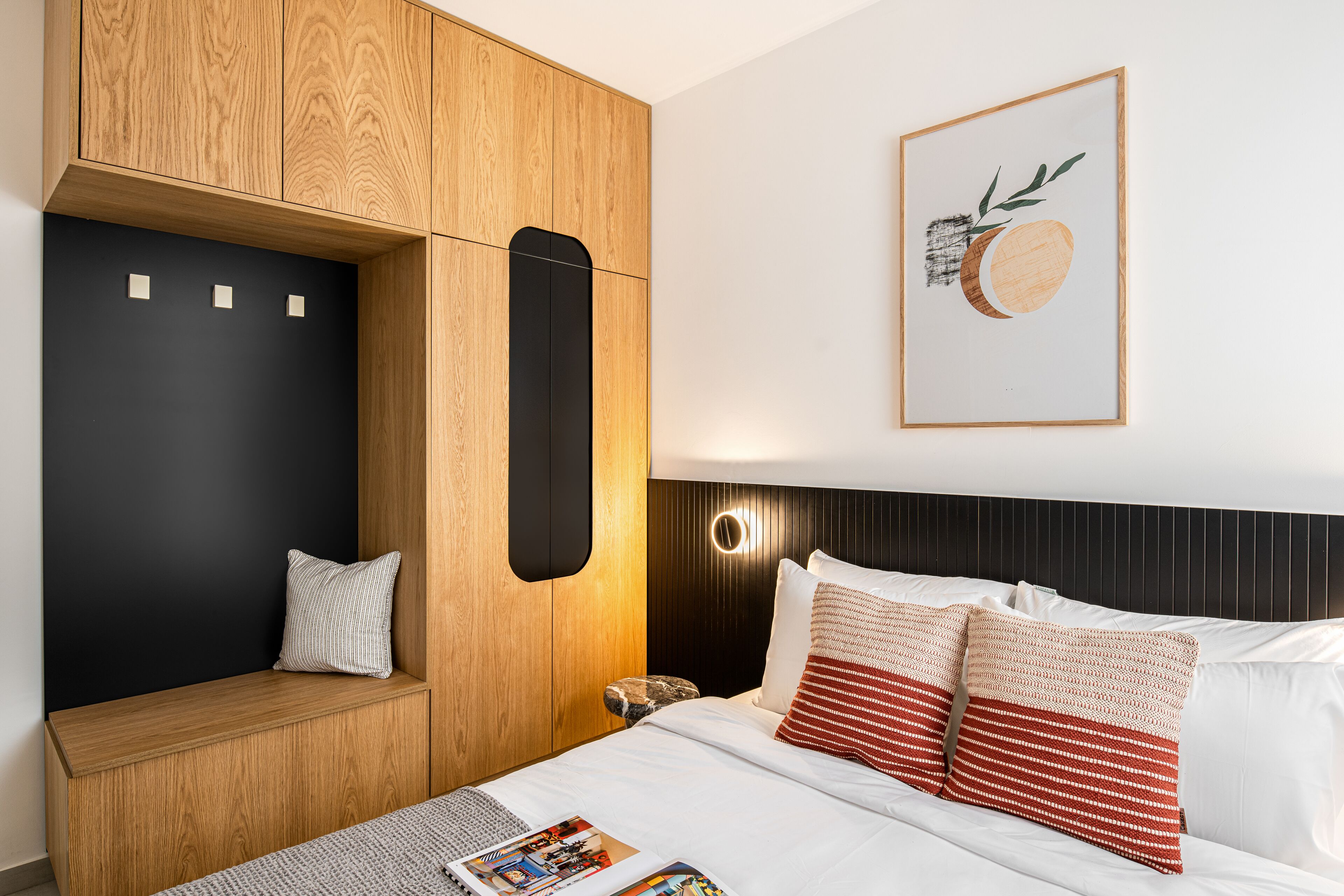 Ein modernes Schlafzimmer mit einem Holzschrank, einer schwarzen Wand als Akzent, einem Bett mit Kissen in Weiß und Rot gestreift sowie einem gerahmten Kunstwerk an der Wand.
