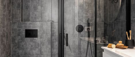 Un baño moderno con ducha de vidrio, inodoro y lavamanos con artículos de aseo.