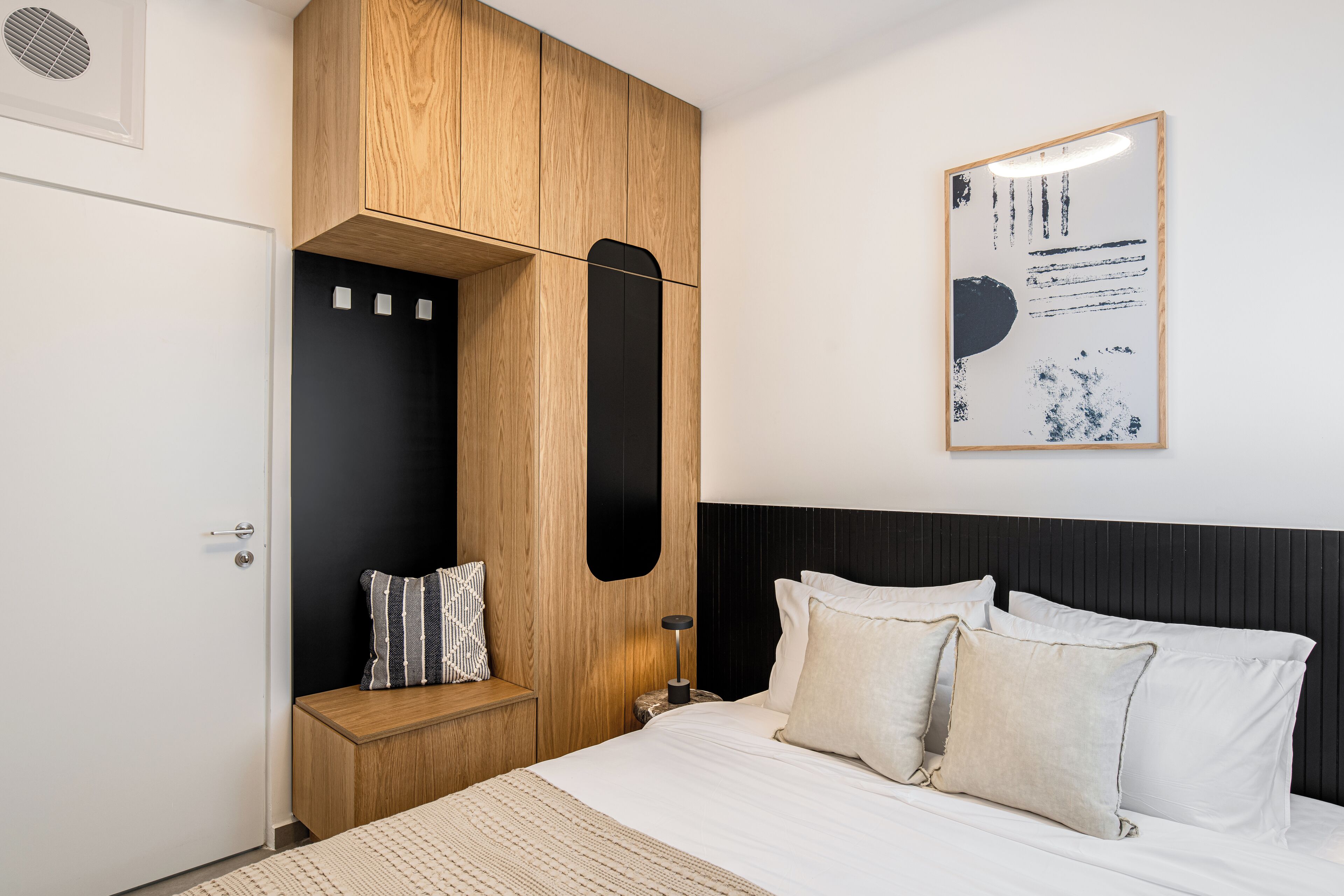 Une chambre à coucher comprenant un lit, une armoire en bois, une table de chevet et une œuvre d’art accrochée au mur.