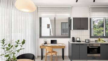 A modern kitchen with a built-in oven, a dining area with a wooden table and chairs, and a large window with blinds.