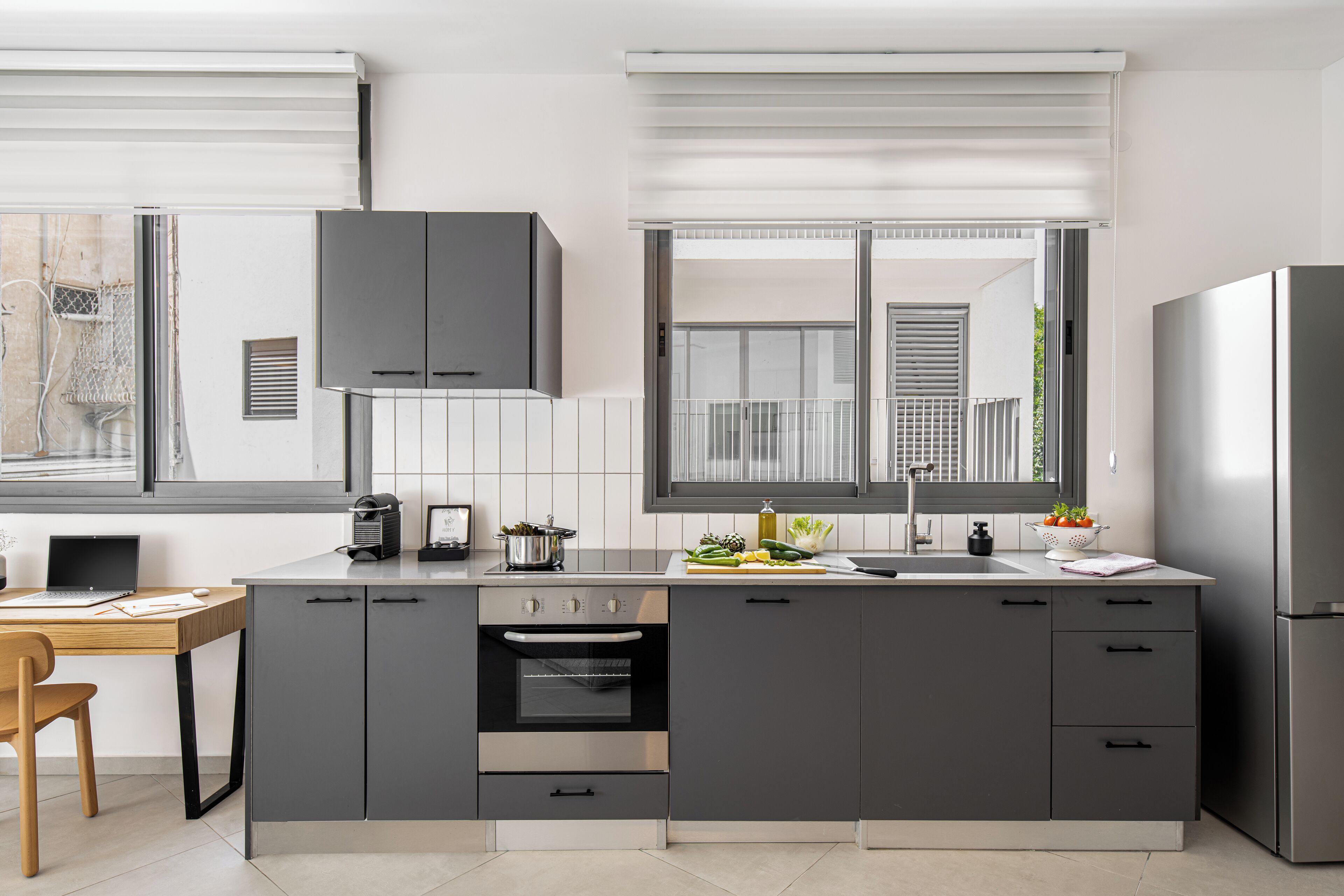 A modern kitchen with grey cabinets, a built-in oven, a sink, and a window with blinds.