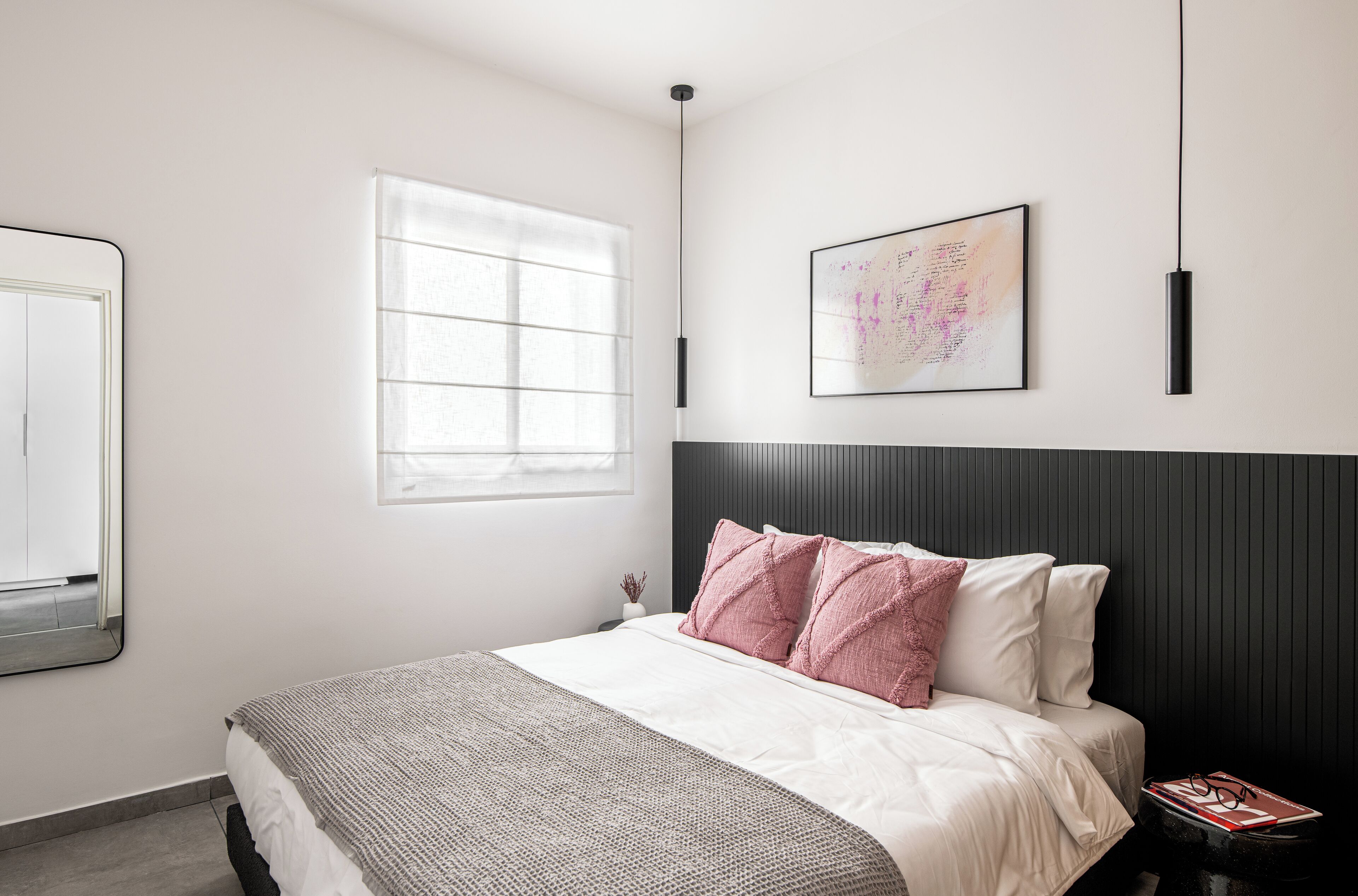 A modern bedroom with a bed, a window, a wall-mounted artwork, and a bedside table with a book and glasses.