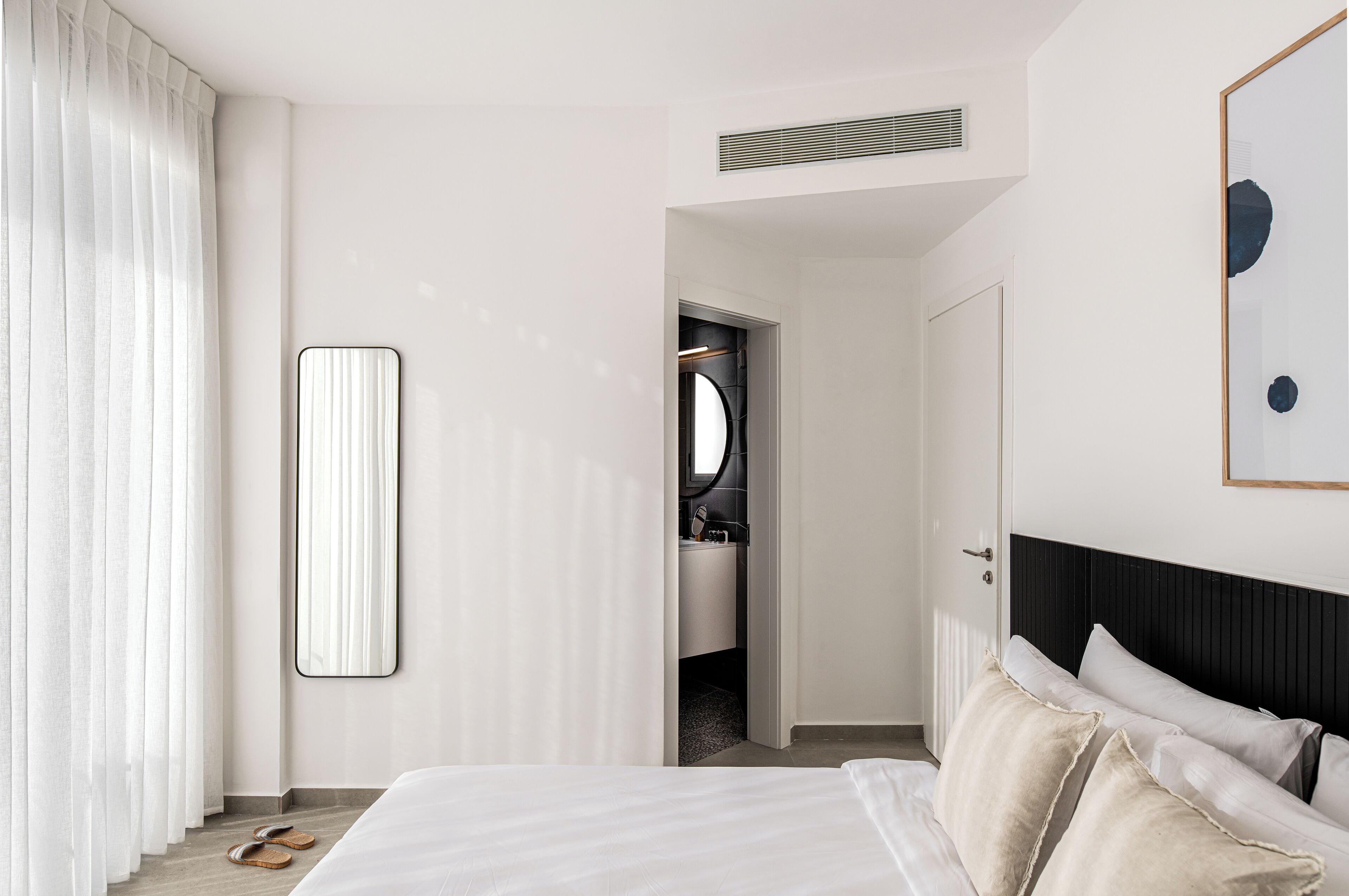 A hotel room with a bed, a mirror, a door leading to a bathroom, and a view of the bathroom.