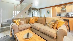 Ein Wohnzimmer mit einem beigefarbenen Ecksofa, einem Holztisch und einer Treppe, die zu einer oberen Etage führt.