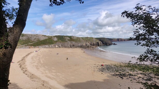 Ein Strand mit sandigem Ufer, felsigen Klippen und blauem Himmel.