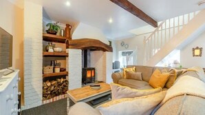 Ein gemütliches Wohnzimmer mit Kamin, Holzbalken, einer Treppe und einem bequemen Sofa.