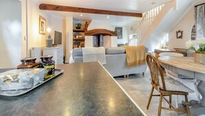 Eine moderne Küche mit Kochinsel, ein Essbereich mit Holztisch und ein gemütlicher Wohnbereich mit Sofa und Treppe.