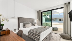 Ein modernes Schlafzimmer mit einem großen Bett, einem Holztisch und Blick auf die Stadt durch raumhohe Fenster.