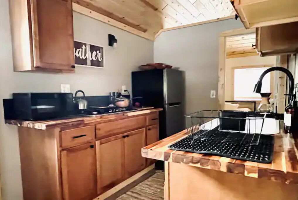 Una cocina compacta con armarios de madera, una encimera negra, un lavamanos y un refrigerador.