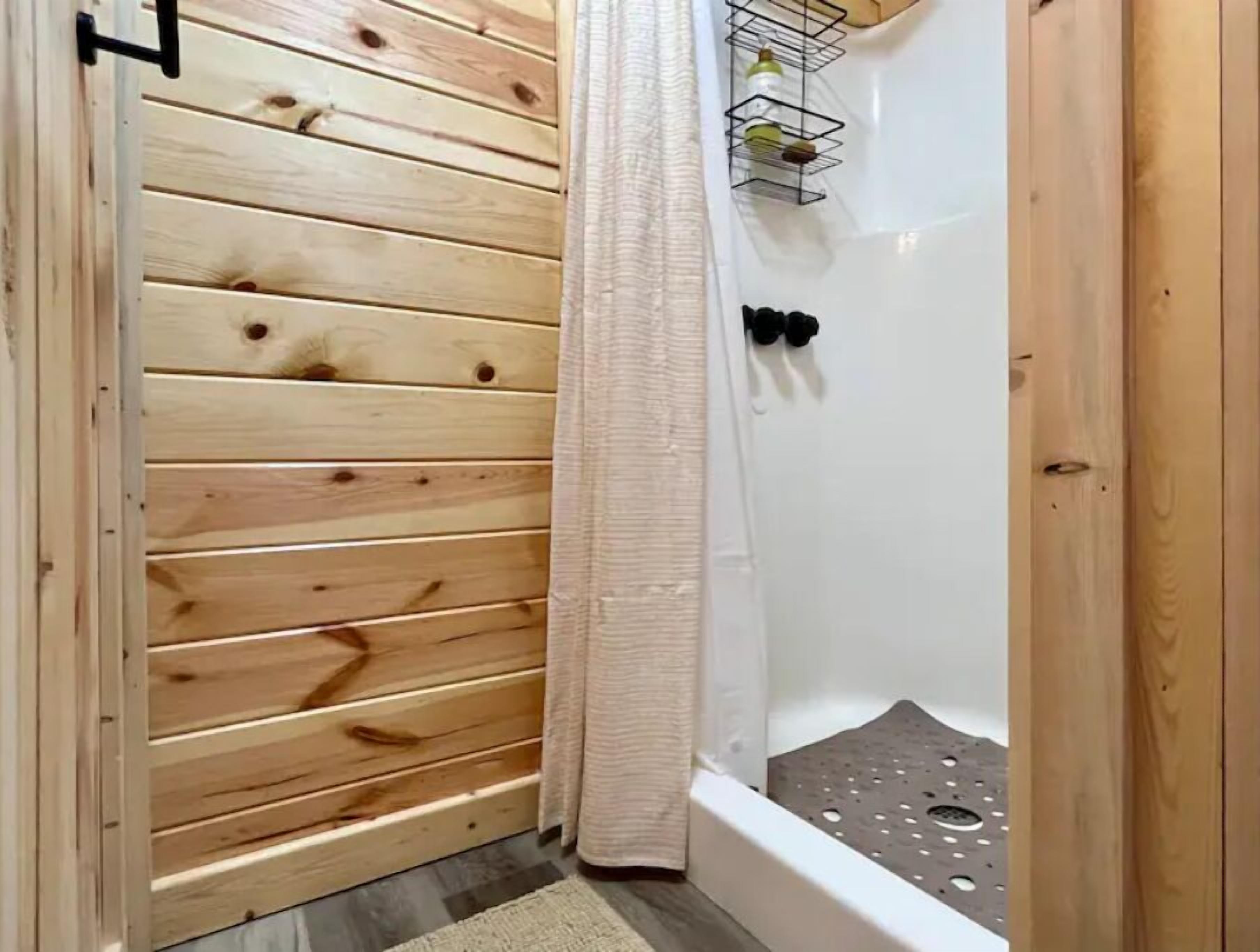 Une salle de bain aux murs lambrissés, comprenant un espace douche, un porte-serviettes et une petite étagère avec des articles de toilette.