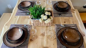 Een houten eettafel met vier borden, twee wijnglazen en een gevlochten mand met bloemen.