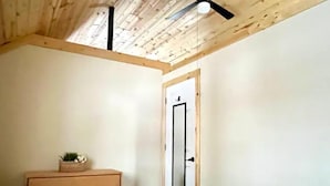 Een slaapkamer met een houten plafond, een witte deur, een houten dressoir en een bed.