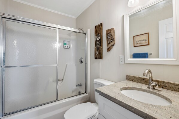 Une salle de bain avec une douche à parois de verre, des toilettes blanches et un lavabo en granit avec un miroir au-dessus.