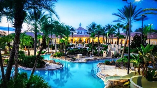 A resort pool area with a large pool, palm trees, and a building in the background. - Spacious & Modern 3BR Townhouse Near Disney w/ Pool & Lazy River! (Davenport)