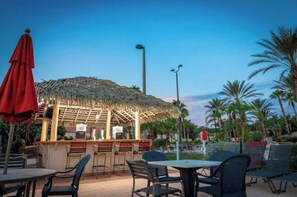 An outdoor dining area with a thatched-roof bar, tables, and chairs. - Spacious & Modern 3BR Townhouse Near Disney w/ Pool & Lazy River! (Davenport)