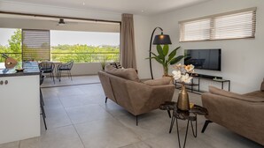 En moderne stue med et fladskærms-tv, behagelige siddepladser, et spiseområde og en balkon med udsigt.