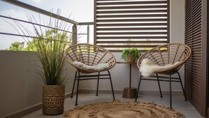 En balkon med to fletstole, et lille bord med en plante, og en potteplante.
