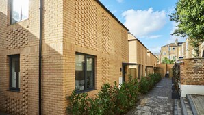 A modern building with a brick facade, a narrow pathway, and a small garden area. - Hammersmith Mews by Viridian Apartments (London)