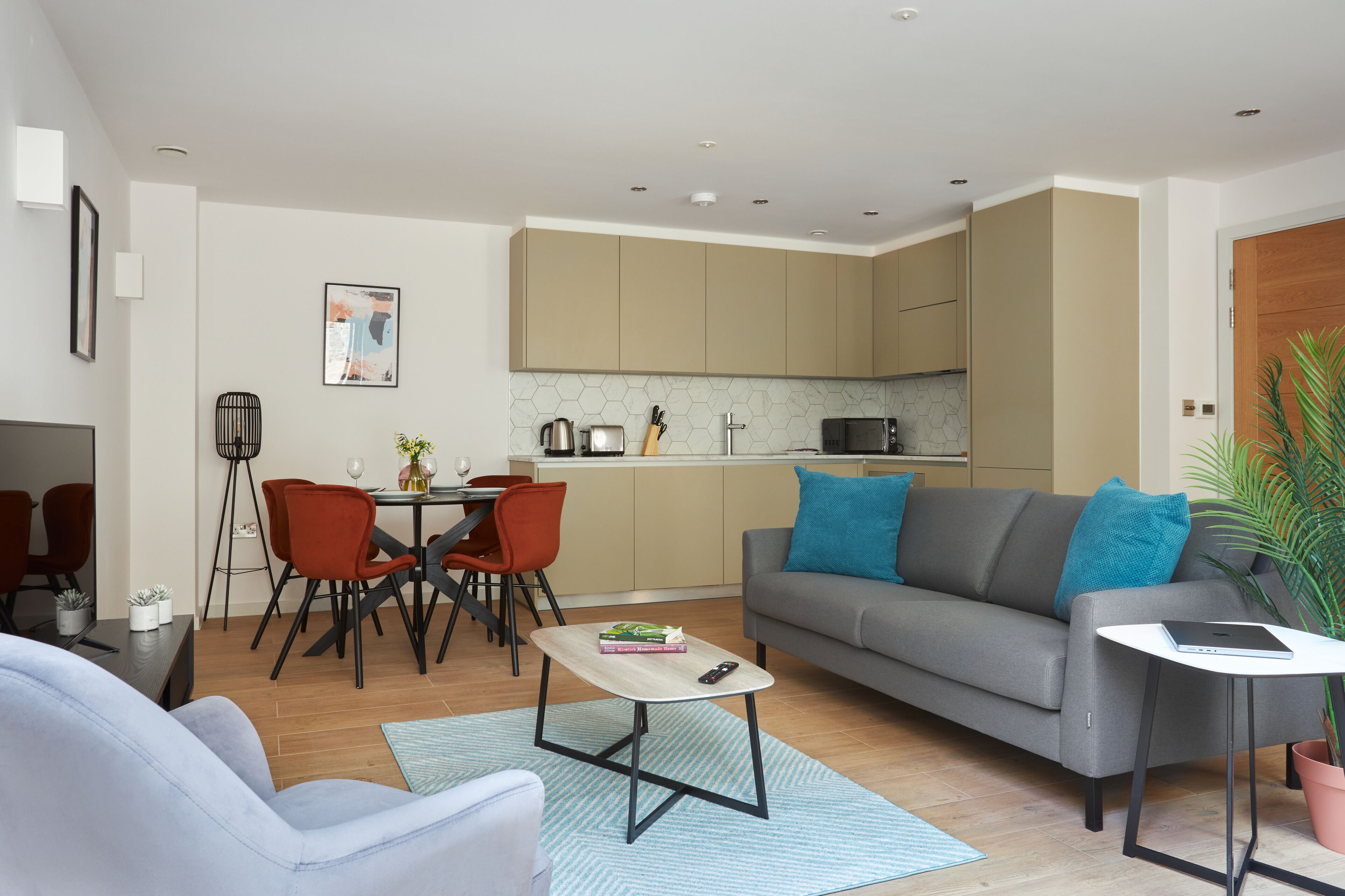 A modern living room with a grey sofa, red chairs, a coffee table, and a dining area with a white table and chairs.