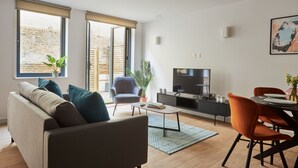 A modern living room with a sofa, armchair, dining table, and TV. - Hammersmith Mews by Viridian Apartments (London)