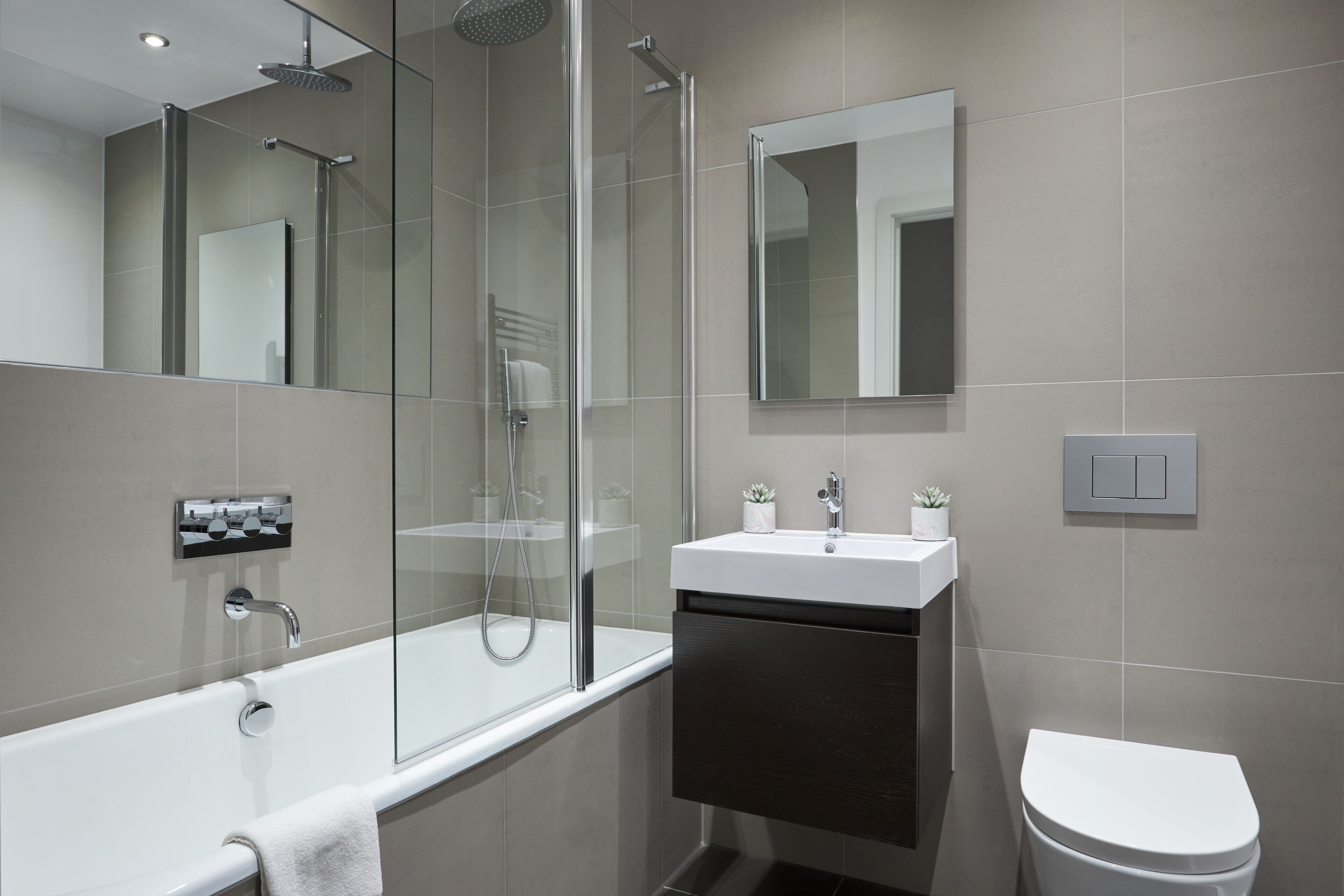 Een moderne badkamer met een douchecabine van glas, een witte badkuip, een wastafel met een spiegel erboven en een toilet.