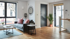 A modern living room with a grey sofa, a small round table, and a potted plant. - Hammersmith Mews by Viridian Apartments (London)