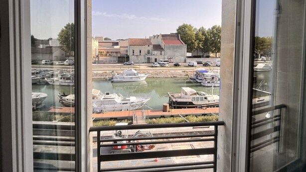 A view from a window overlooking a marina with boats, a building in the background, and a clear sky.