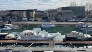 A marina with boats docked, a road with cars, and buildings in the background.